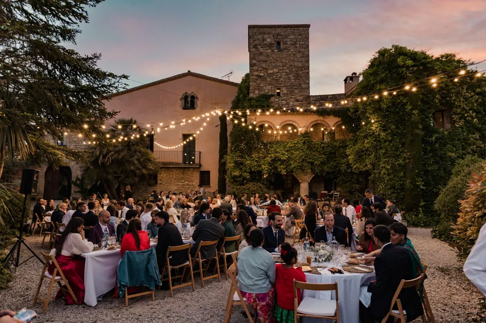 Cena al atardecer bajo guirnaldas de luces en el patio de una masía