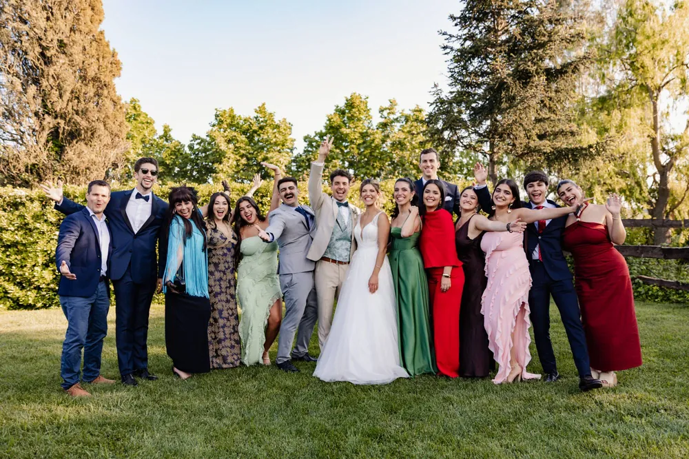 Los novios con sus amigos en el jardín, todos con los brazos en alto