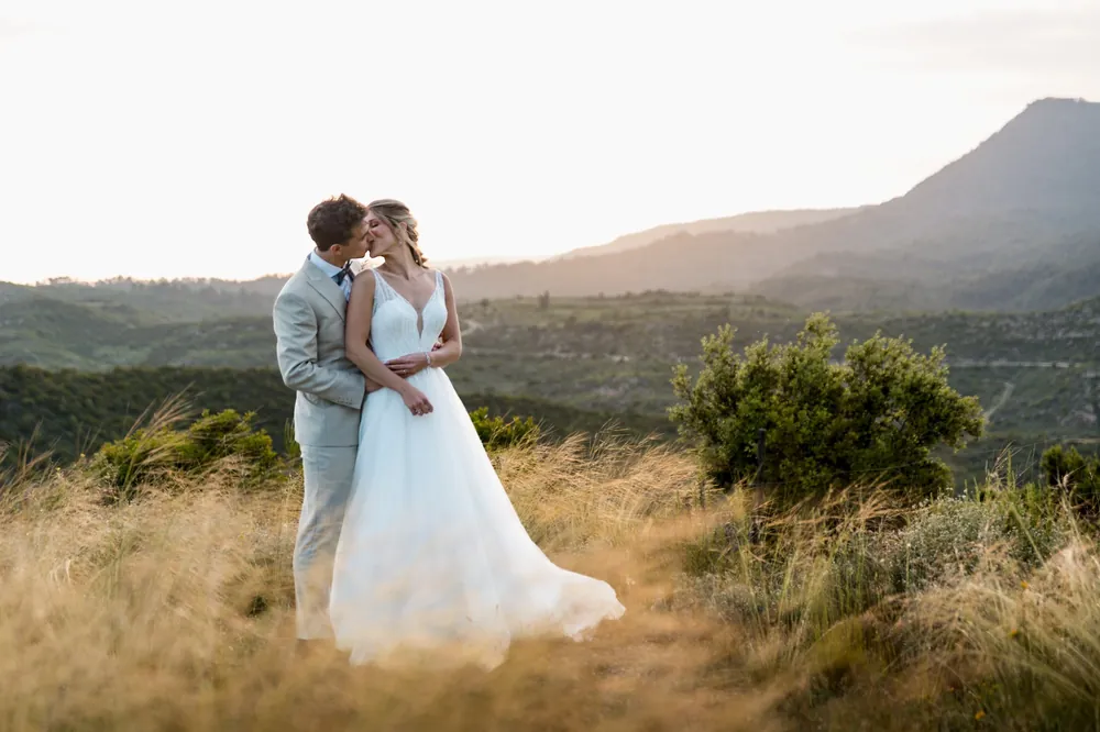 Los novios se besan al atardecer en un prado de hierba alta frente a las montañas